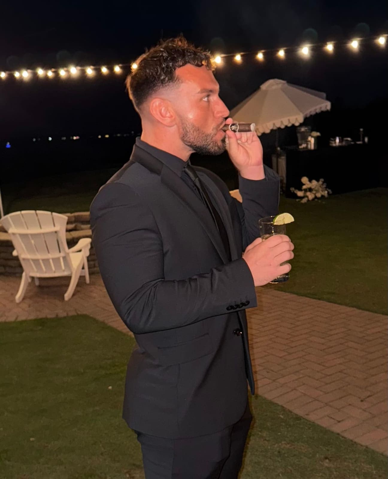 Man in black suit enjoying a cigar and cocktail at an evening event