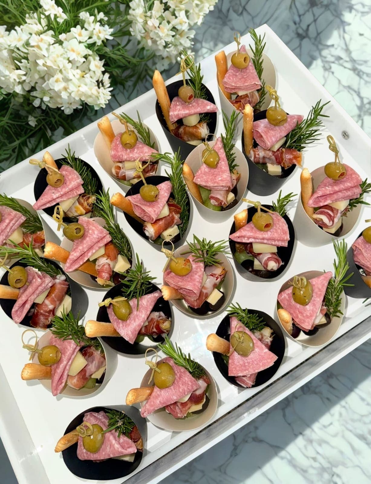 Individual charcuterie cups with salami, olives, and rosemary