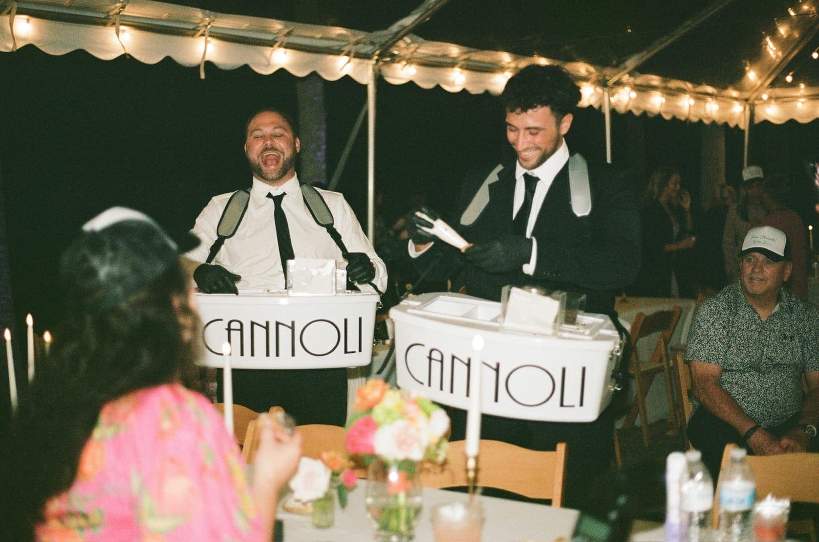 Two cannoli cart servers entertaining guests at a tent reception
