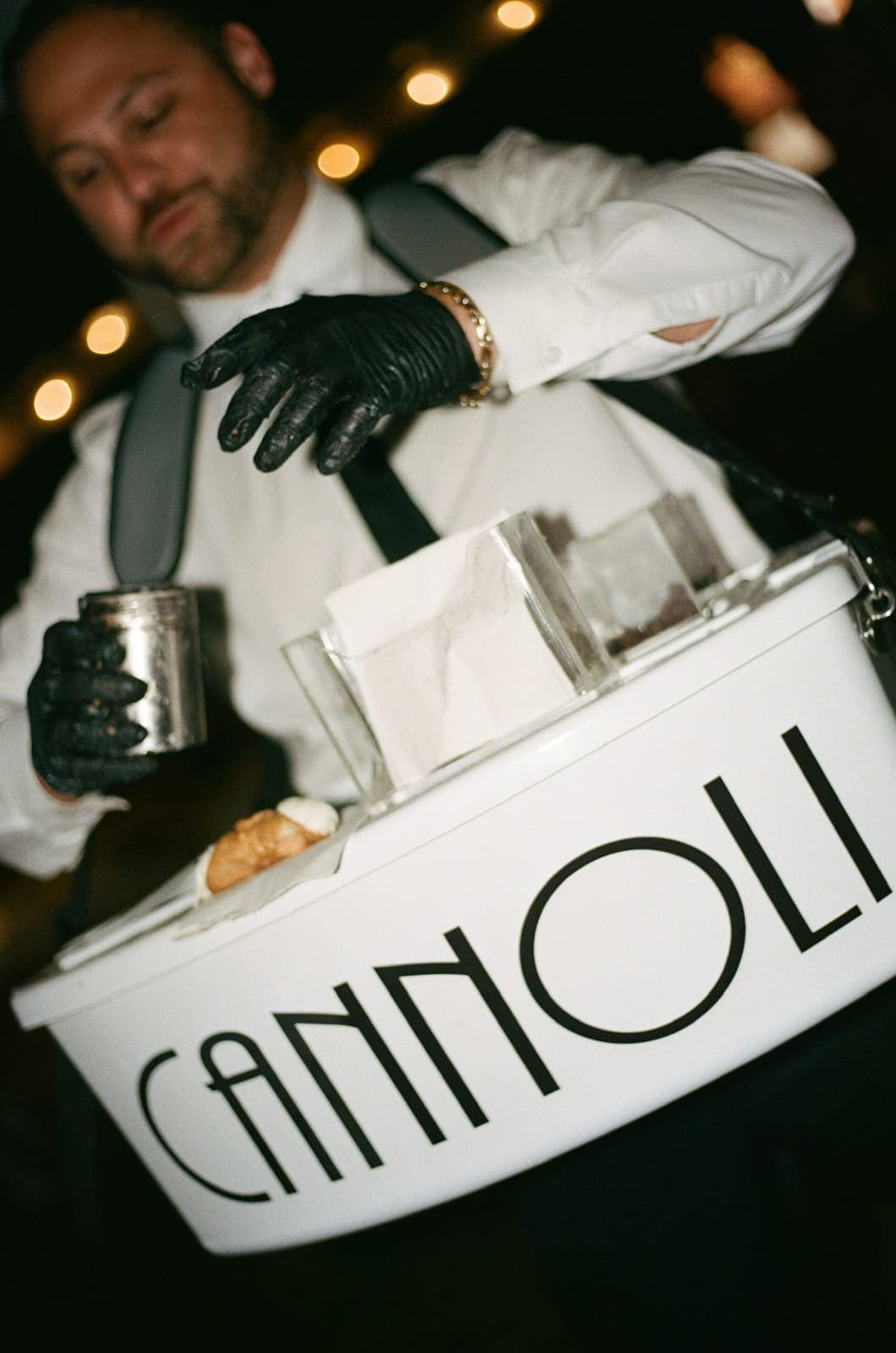 Close-up of a cannoli cart server dusting toppings at night