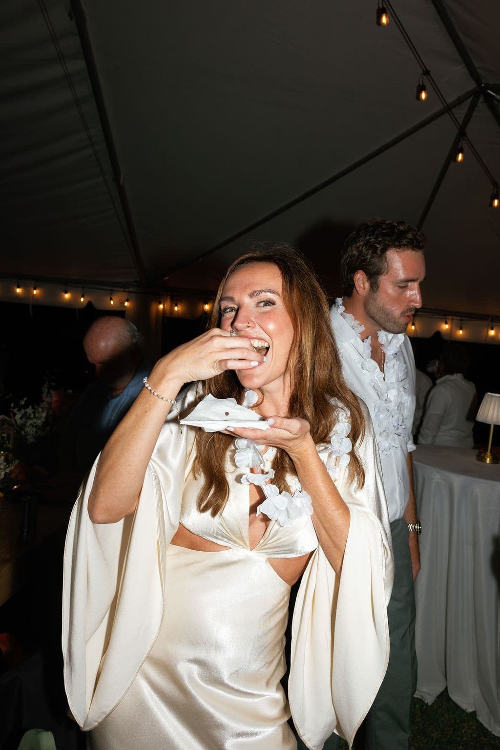 Bride laughing while enjoying a cannoli under the reception tent