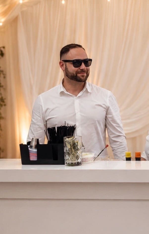 Bartender in sunglasses behind the bar at a draped tent event