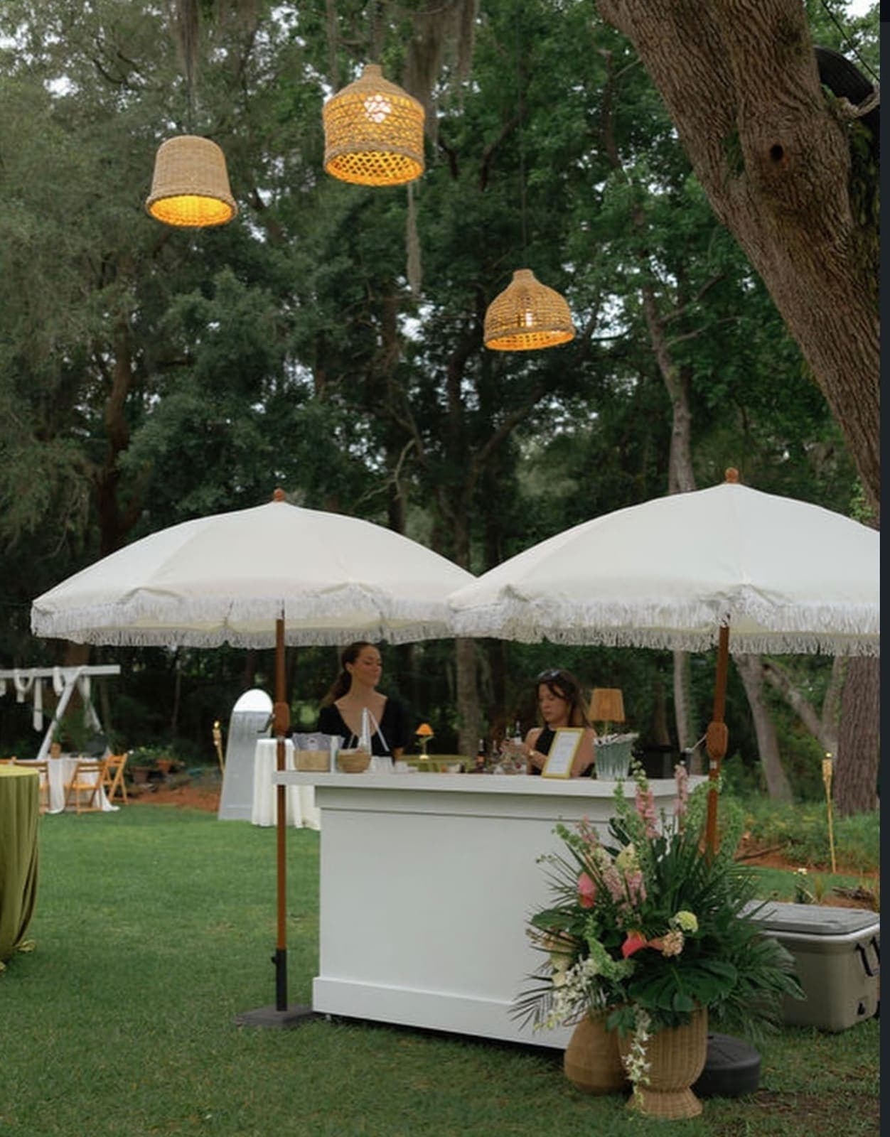Two bartenders serving under white fringe umbrellas outdoors