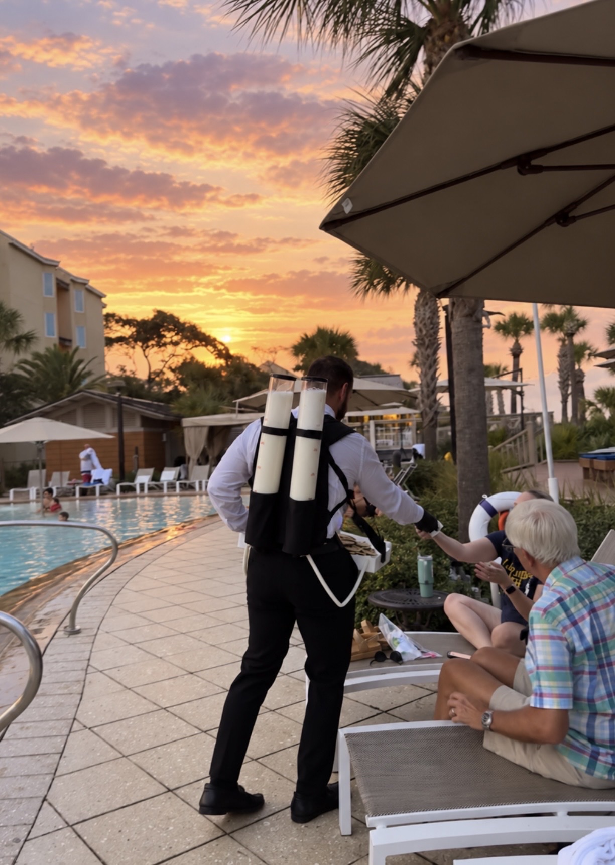Bottoms Up Luxury attendant serving chilled milk shooters to guests poolside at sunset