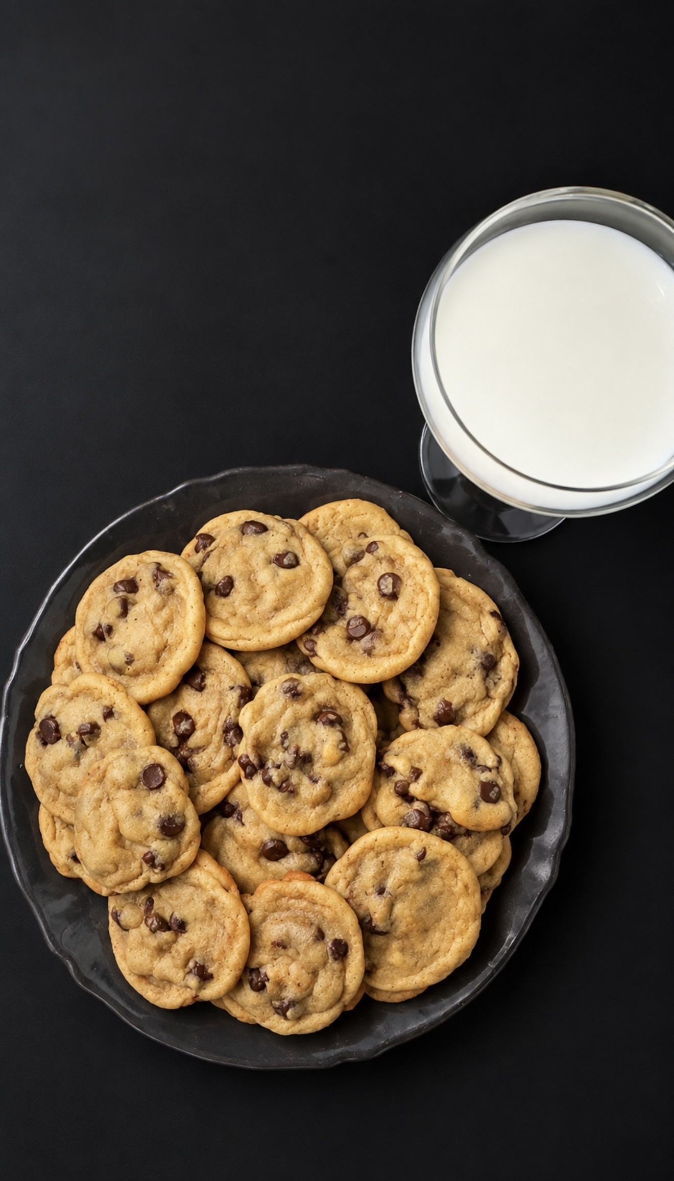 A platter of freshly baked chocolate chip cookies beside a chilled glass of milk